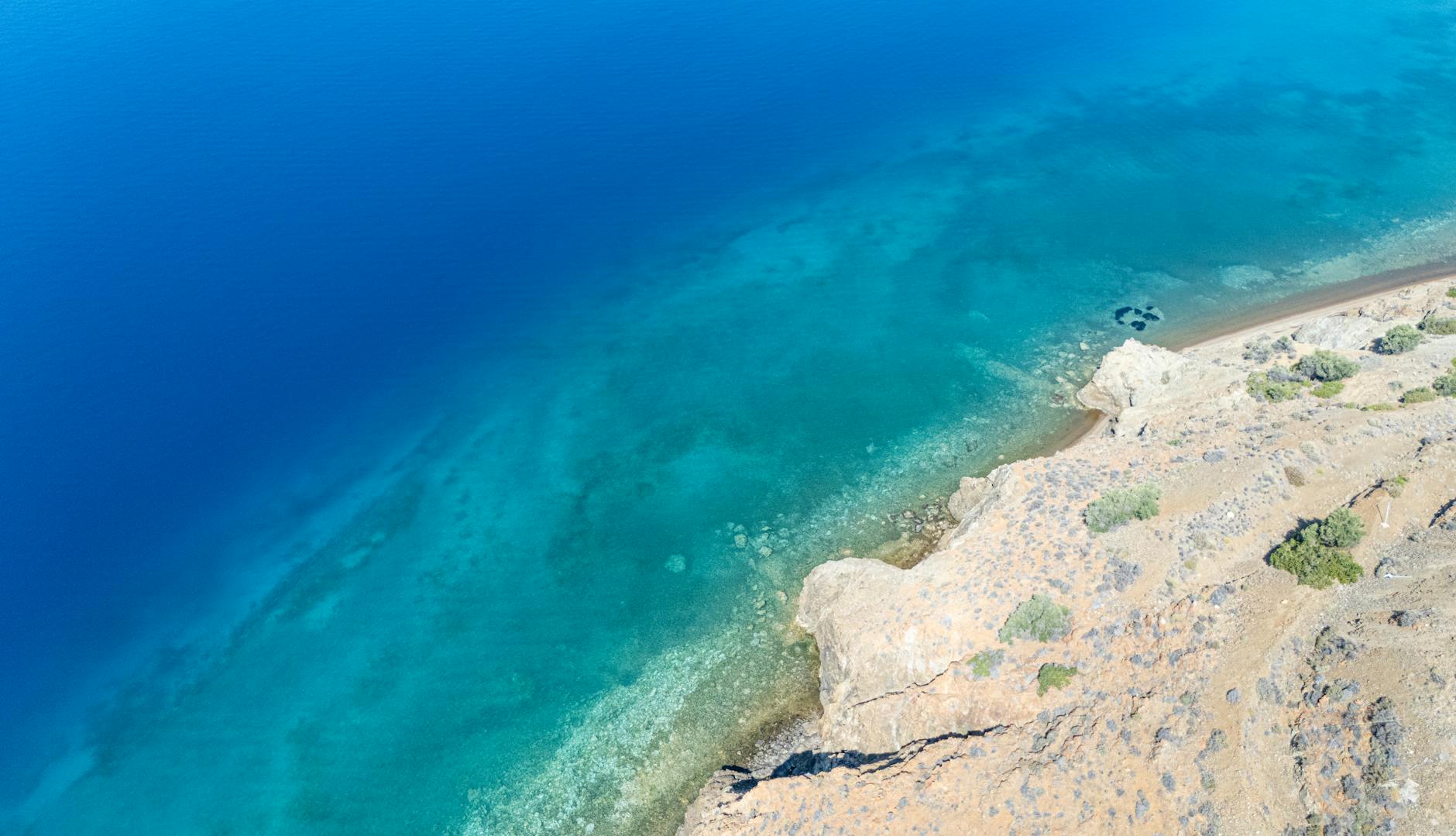 Stunning aerial view of rocky shoreline with clear turquoise waters in Greece.