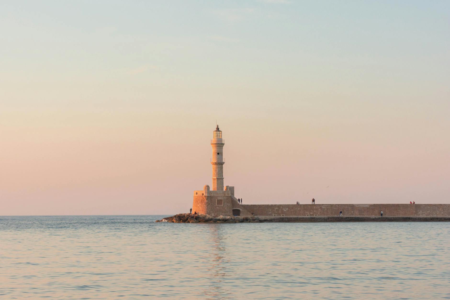 Serene view of the Chania Lighthouse in Crete against a calm sea at sunrise.