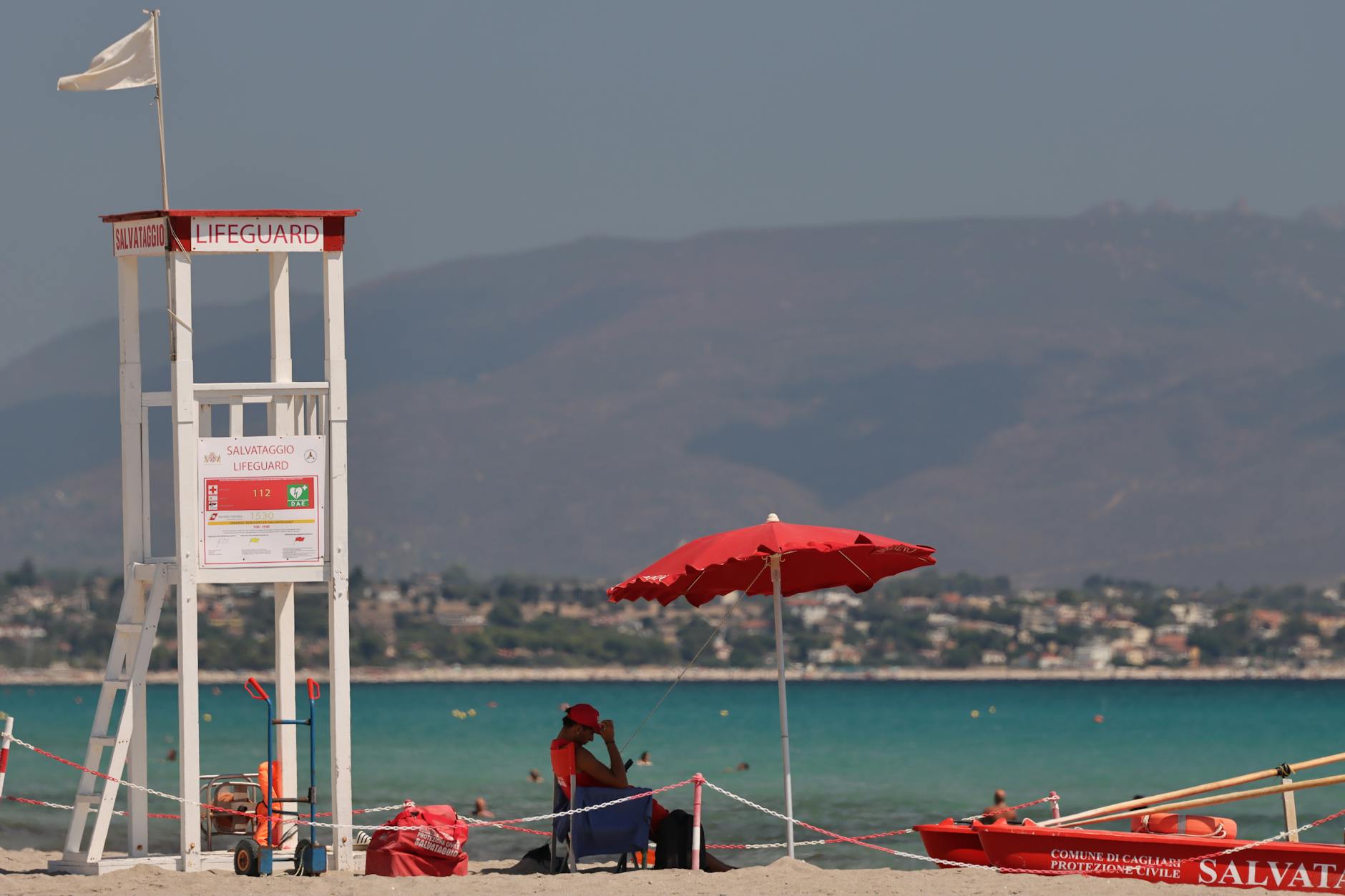 Lifeguard tower with red umbrella at Sardegna beach, Italy, highlighting vibrant summer vibes.