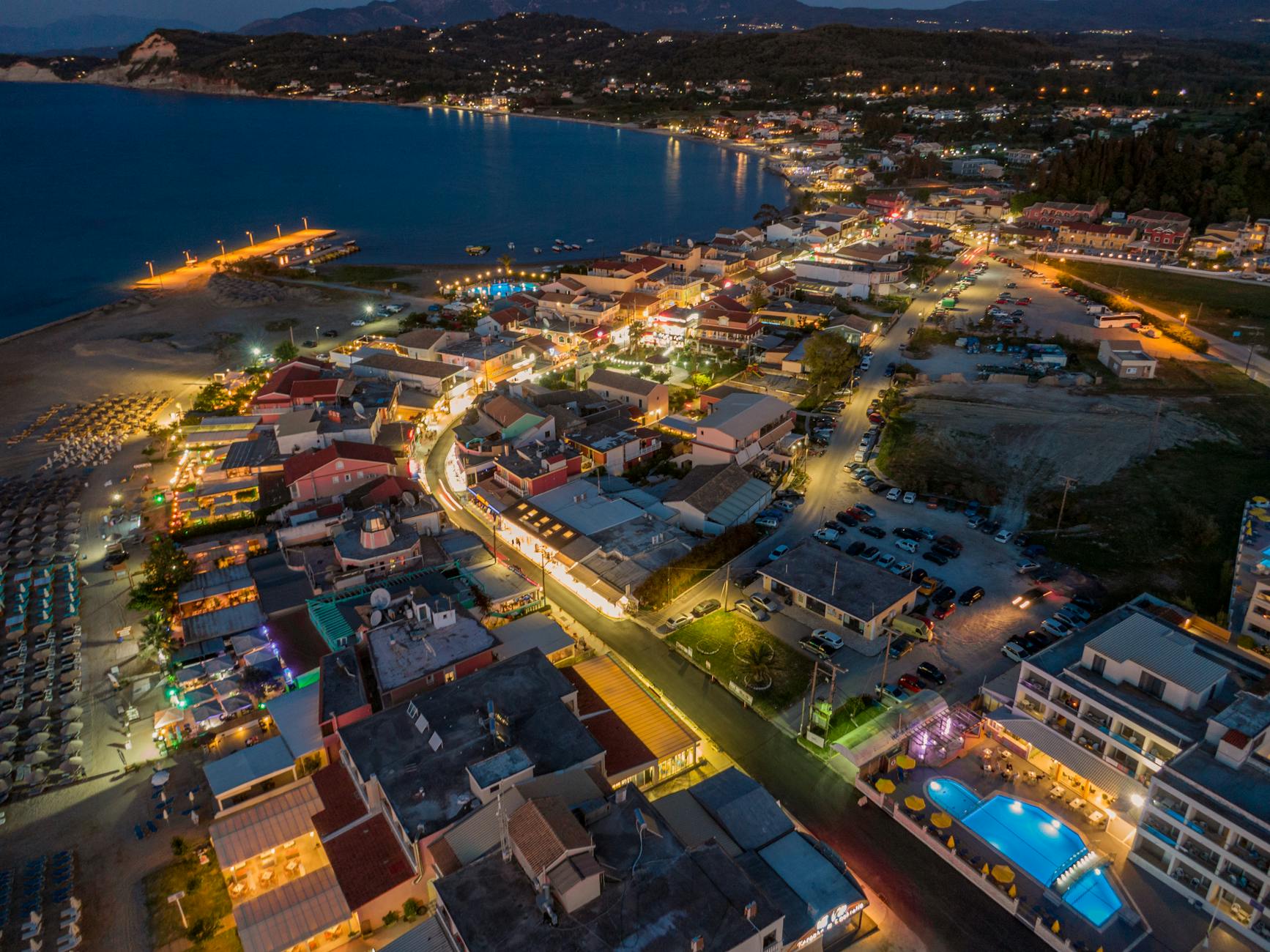 A captivating aerial view of Sidari, Greece, highlighting its vibrant coastal nightlife and illuminated cityscape.