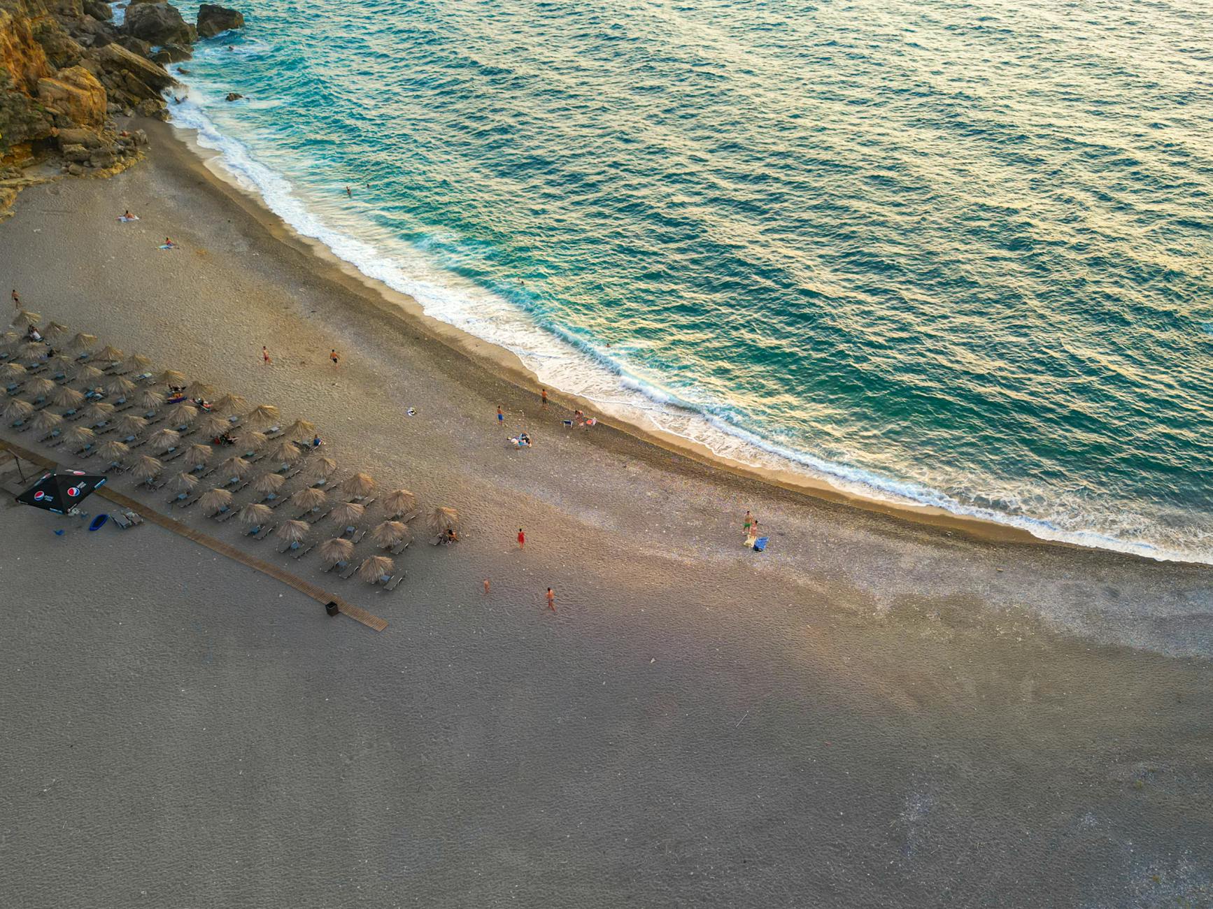 A tranquil aerial shot of a beach in Crete with turquoise waters and parasols at sunset, perfect for vacation inspiration.
