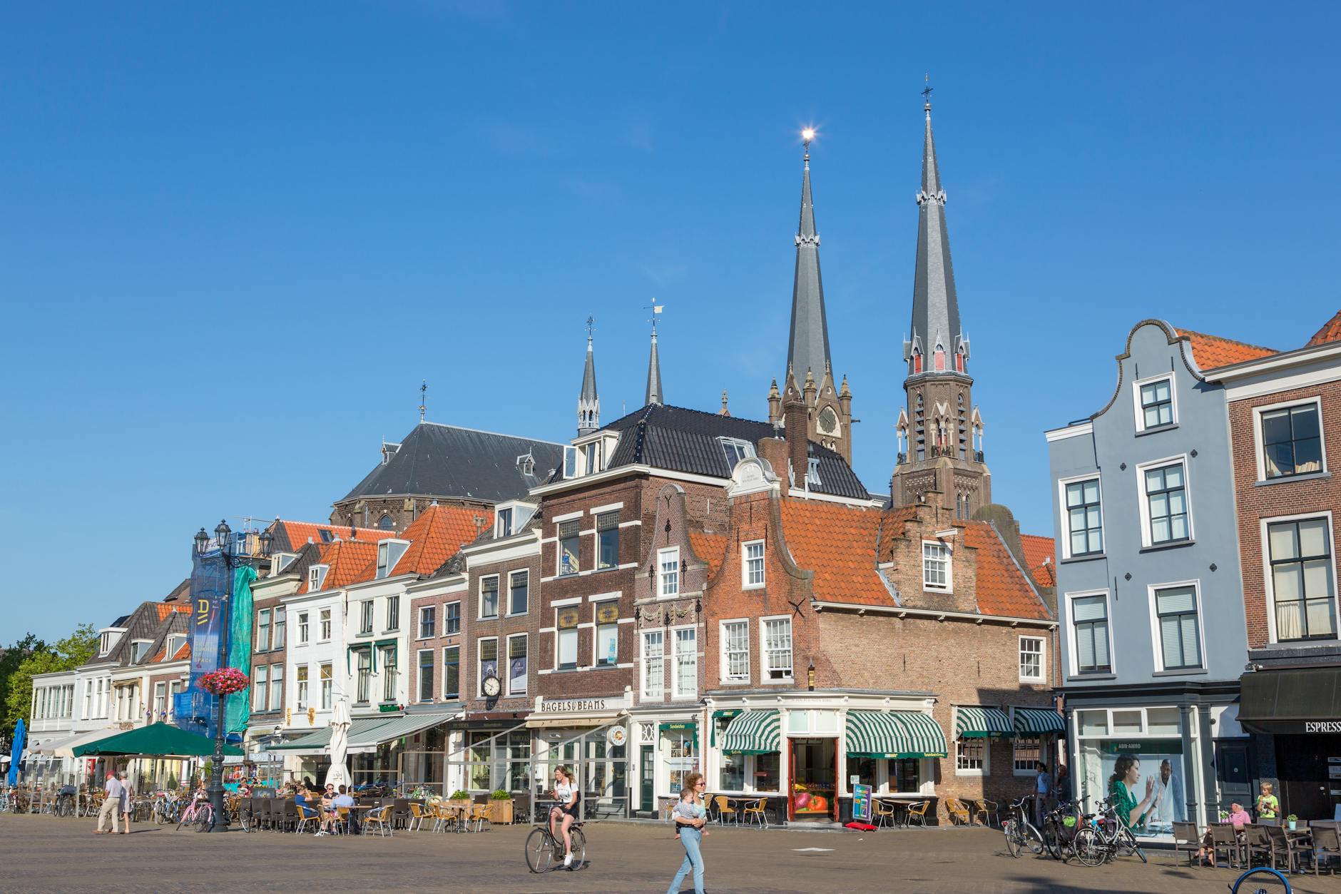 A vibrant scene in a Dutch square featuring historical buildings and a church under a clear blue sky.