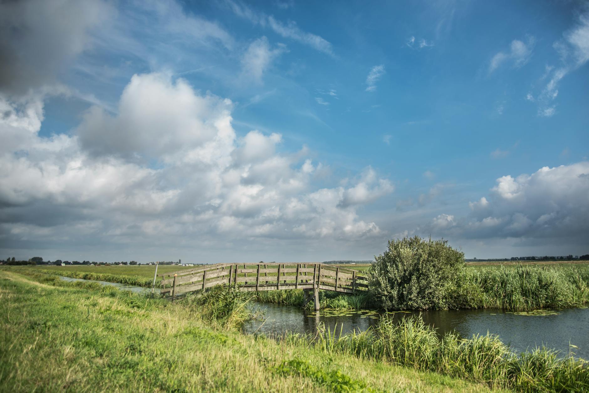 Tranquil rural landscape featuring a wooden bridge, fields, and dramatic clouds in the Netherlands.