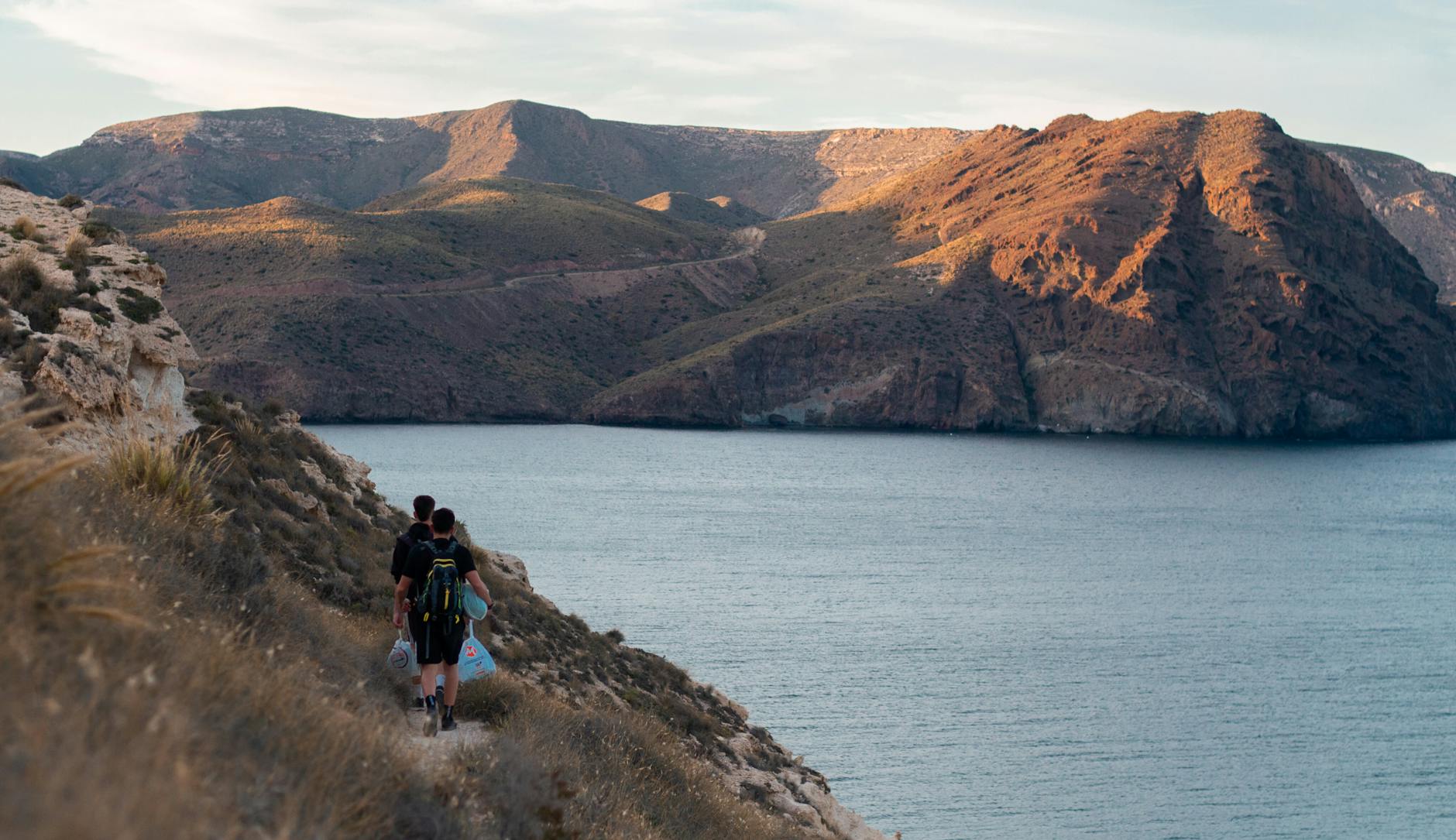 Two hikers traverse a coastal trail with stunning mountain and ocean views.