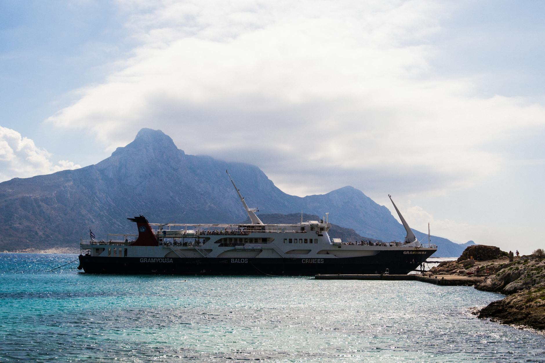 Ferry docked at the picturesque Balos Beach, Greece with a mountainous backdrop.